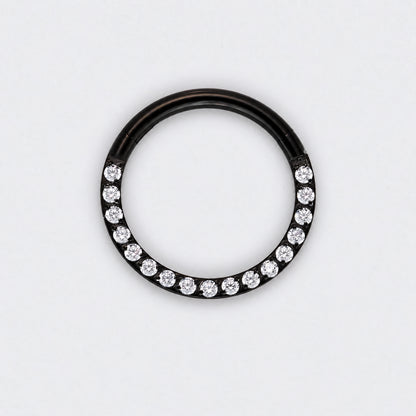 A black metal ring featuring a row of clear round-cut gemstones along the lower half, photographed against a plain white background.