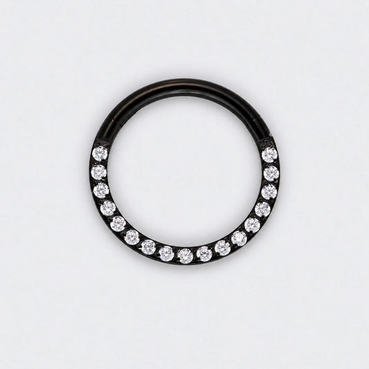 A black metal ring featuring a row of clear round-cut gemstones along the lower half, photographed against a plain white background.