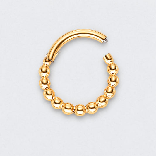 A gold huggie hoop earring featuring a textured, beaded design along the lower curve, shown on a light gray background.