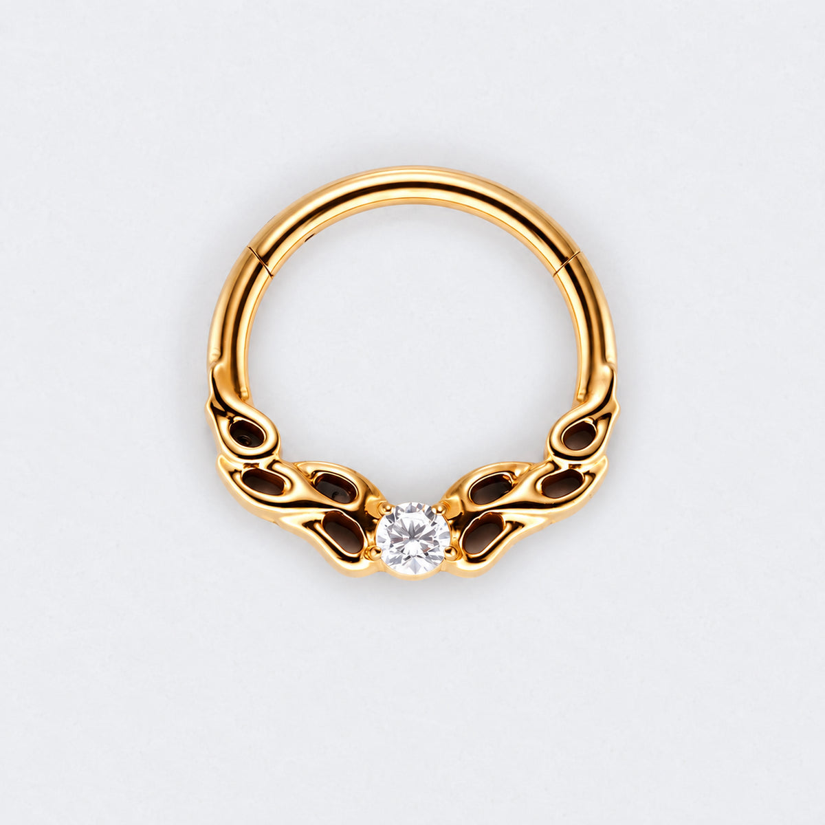 A gold-plated curved hoop piercing ring with decorative scrollwork on the sides and a single clear round-cut gemstone at the center, shown on a light gray background.