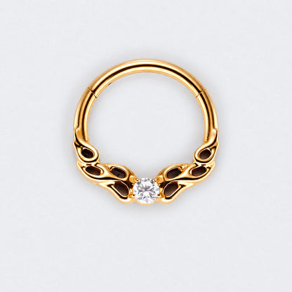 A gold-plated curved hoop piercing ring with decorative scrollwork on the sides and a single clear round-cut gemstone at the center, shown on a light gray background.