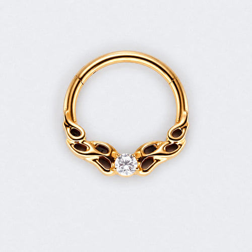 A gold-plated curved hoop piercing ring with decorative scrollwork on the sides and a single clear round-cut gemstone at the center, shown on a light gray background.
