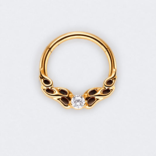 A gold-plated curved hoop piercing ring with decorative scrollwork on the sides and a single clear round-cut gemstone at the center, shown on a light gray background.